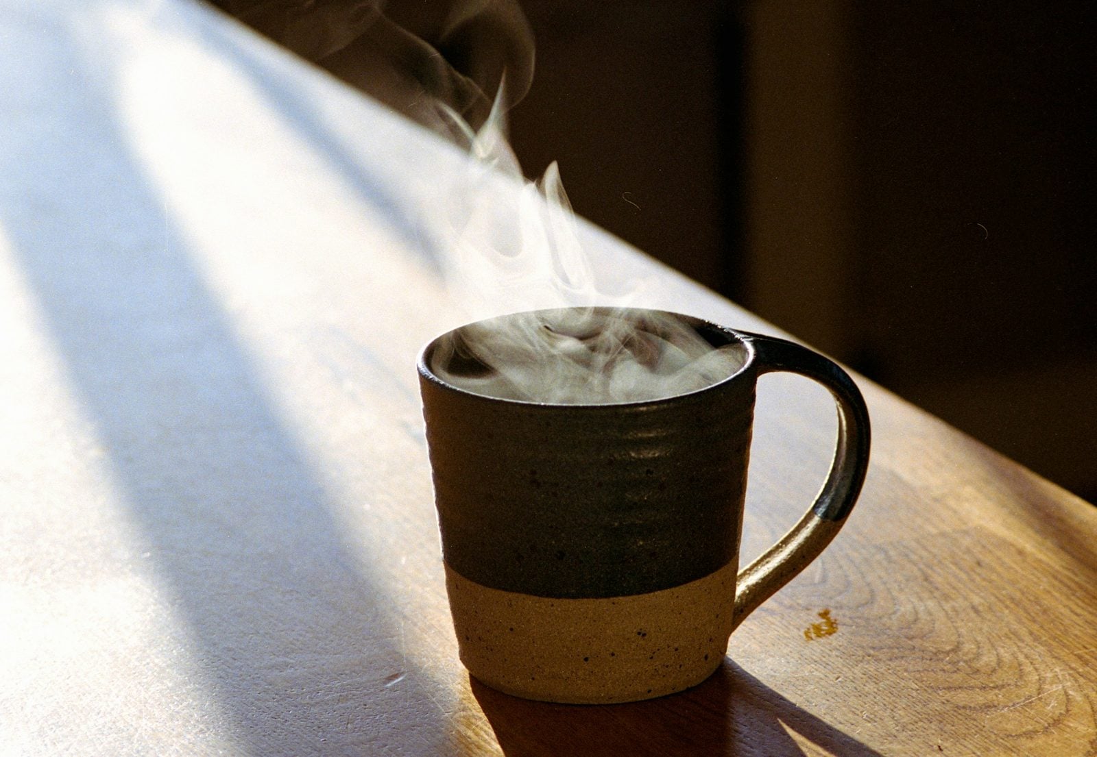 A steaming stoneware mug on a sunlit wooden counter