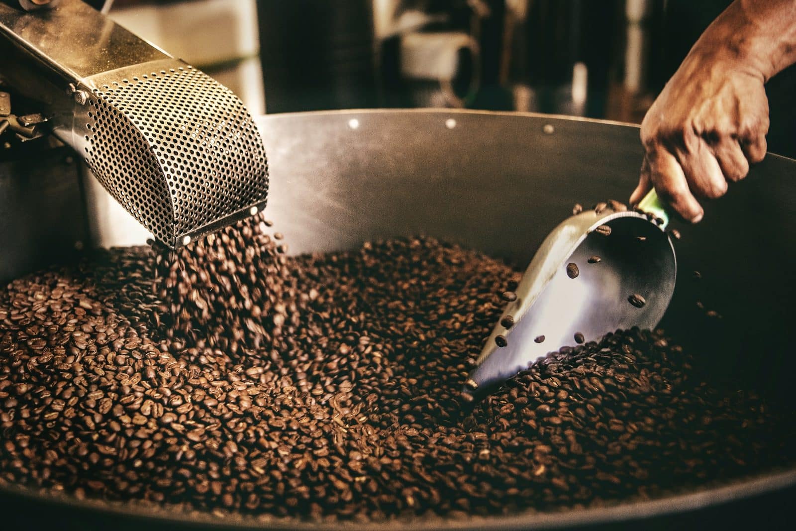 Hand and scoop stirring freshly roasted beans in a cooling tray